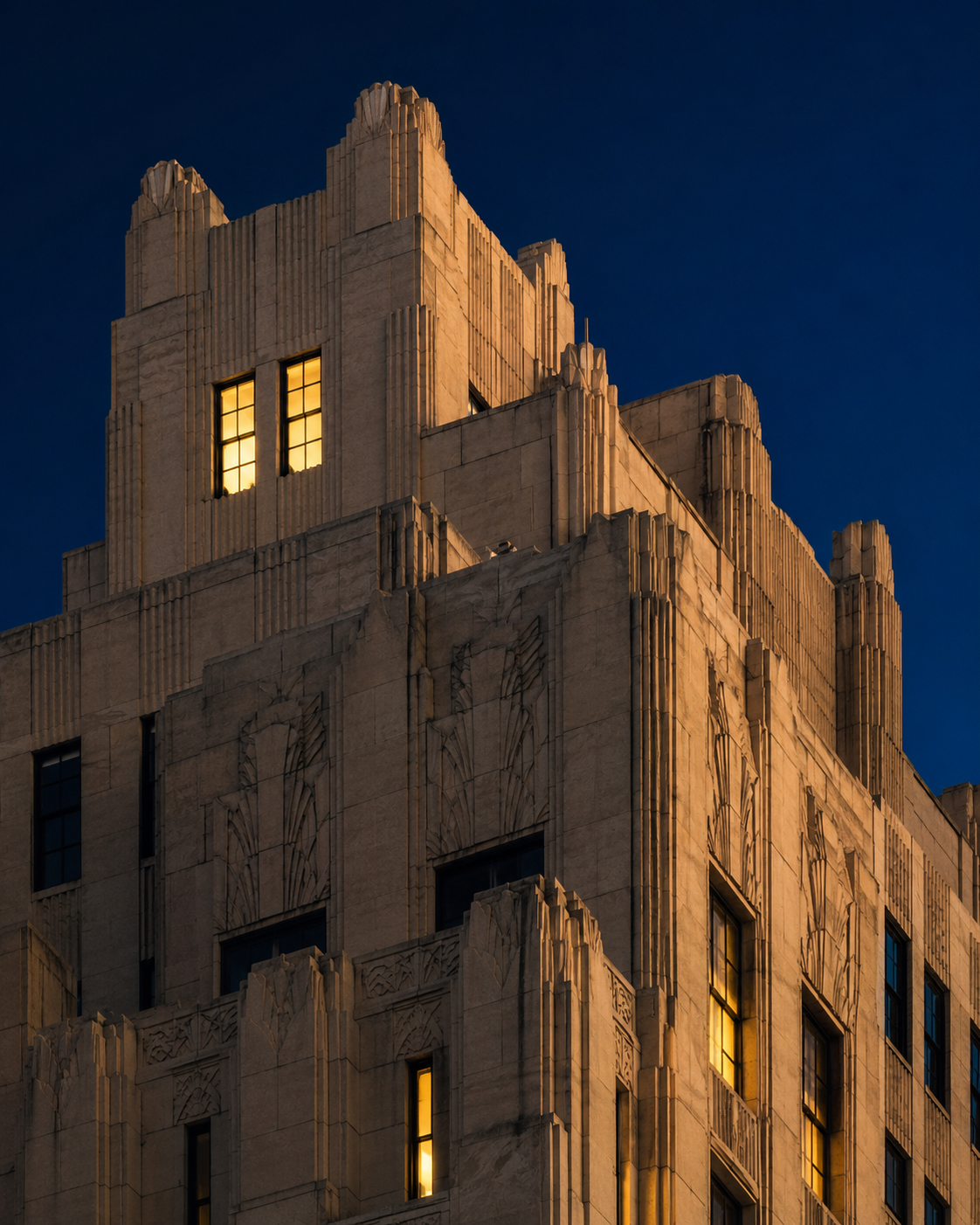 A Manhattan art-deco building at dusk, two windows glowing warmly against a deep navy sky